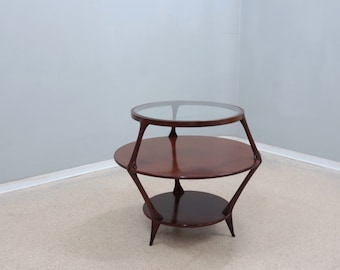 May include: A round, two-tiered table with a glass top and a dark wood base. The table has a unique, geometric design with curved legs.