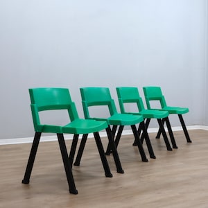 May include: Four green plastic chairs with black legs are arranged in a row. The chairs have a simple design with a seat, back, and four legs. The chairs are set against a light gray wall and a light brown floor.