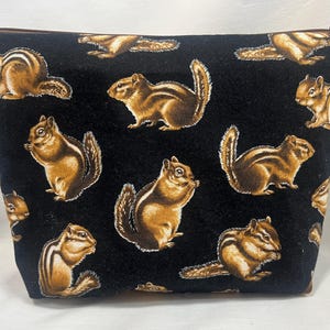 May include: A black zippered pouch featuring a repeating pattern of brown and white chipmunks. The chipmunks are in various poses against a black background. The pouch has a brown zipper.