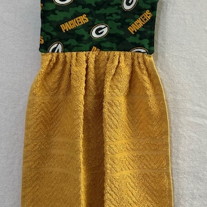 May include: A yellow kitchen towel with a green and white fabric loop featuring the Green Bay Packers logo and the word "Packers" repeated.