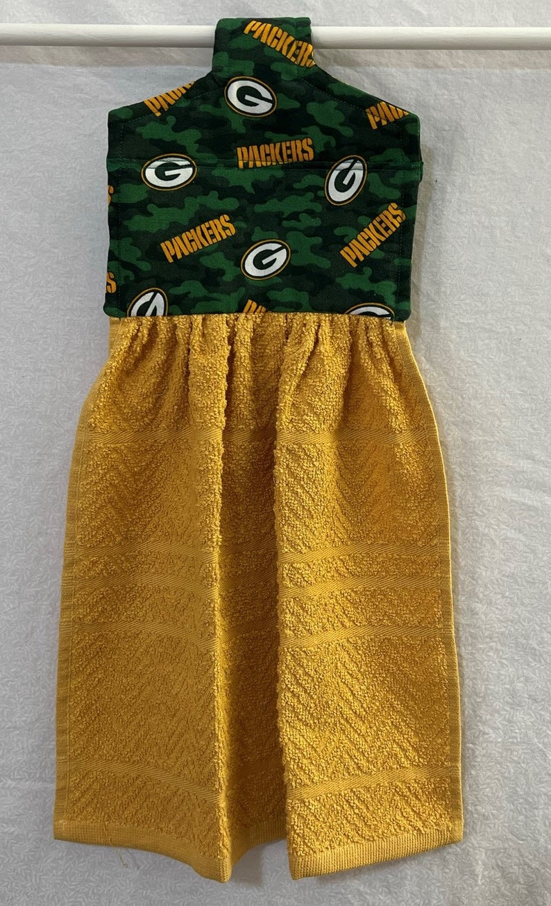 May include: A yellow kitchen towel with a green and white fabric loop featuring the Green Bay Packers logo and the word "Packers" repeated.