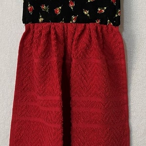 May include: Red and black kitchen towel with a floral print. The towel has a loop for hanging and a textured design.