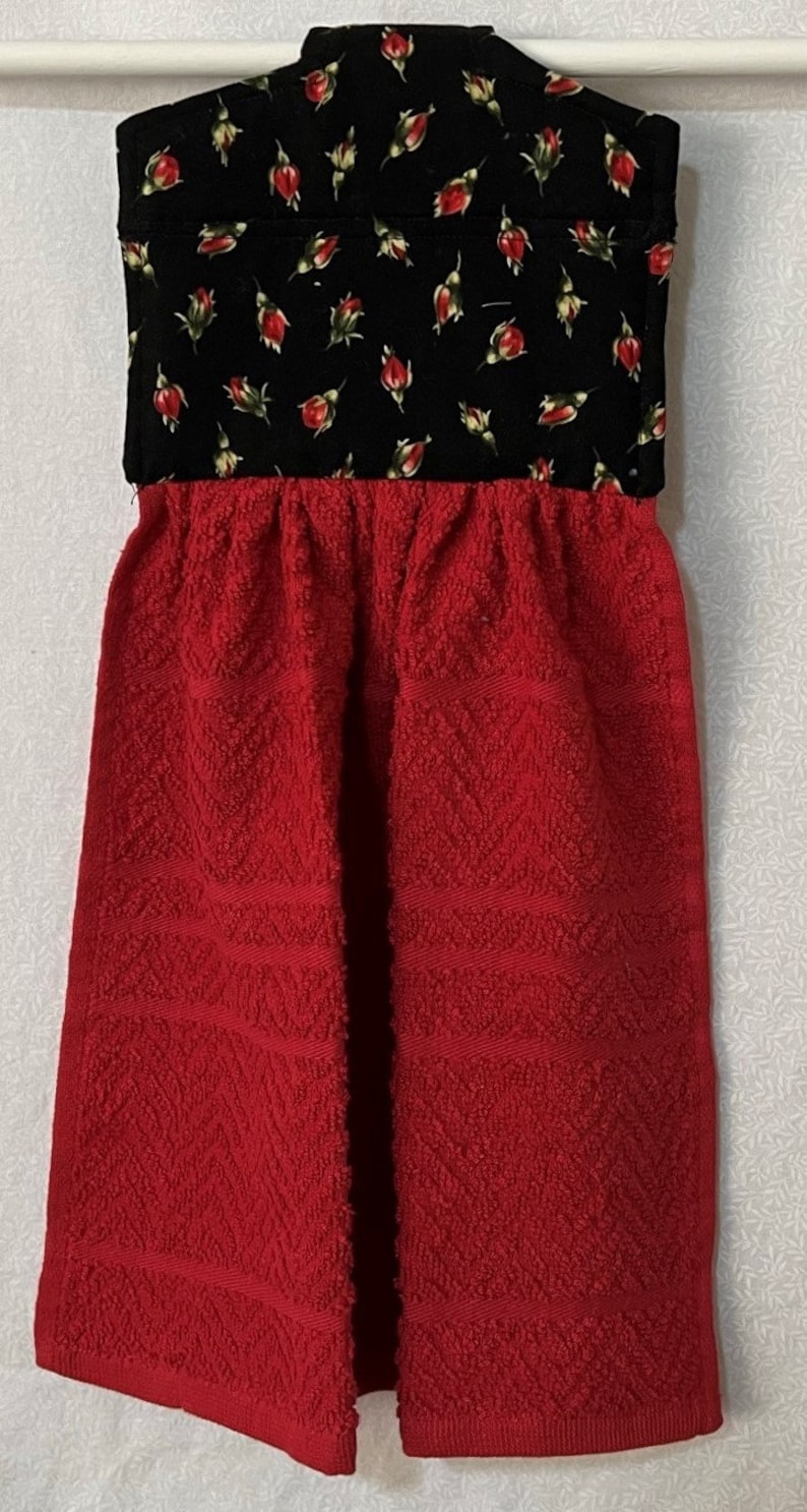 May include: Red and black kitchen towel with a floral print. The towel has a loop for hanging and a textured design.