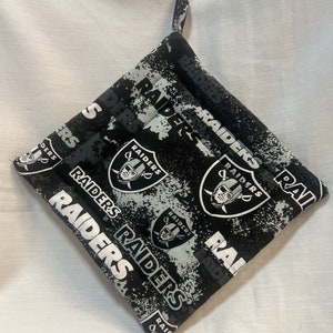 May include: Black and white pot holder with a repeated pattern of the Las Vegas Raiders logo and the word "RAIDERS".
