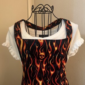 May include: A black and orange sleeveless overall dress with a flame pattern and a skull design. The dress is on a white mannequin.