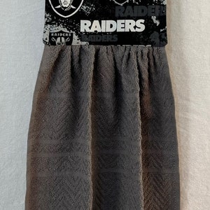 May include: A gray kitchen towel with a black and white pattern featuring the Las Vegas Raiders logo and the word "Raiders".