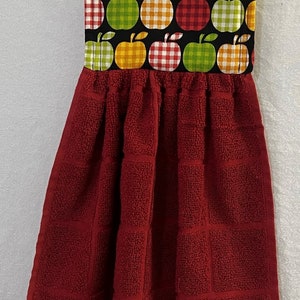 May include: Red kitchen towel with a hanging loop. The top of the towel is decorated with a black fabric with a pattern of green, yellow, and red apples with white gingham.