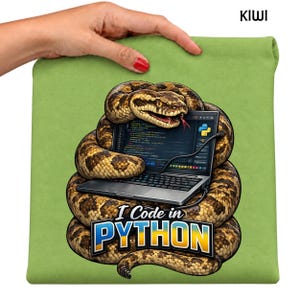 May include: A light green t-shirt featuring a graphic of a brown patterned snake coiled around a silver laptop. The screen displays code and a Python logo. Below the snake, the text reads I Code in PYTHON in bold blue and yellow letters.