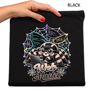 May include: A black t-shirt featuring a graphic of a cute, fuzzy spider wearing glasses and typing on a laptop. The spider is centered in a glowing, colorful spiderweb with lines of computer code. The text Web Master is printed below in white.