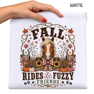 May include: A white sweatshirt featuring a graphic print of a brown and white horse behind a wooden fence. The design includes the text FALL RIDES & FUZZY FRIENDS, surrounded by autumn leaves, sunflowers, pumpkins, horseshoes, and rope accents.