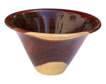 May include: A polished wooden bowl featuring a wide, flared rim and a deep, conical shape. The exterior and interior display a striking contrast between dark, rich mahogany-toned wood grain and lighter, natural cream-colored wood sections.