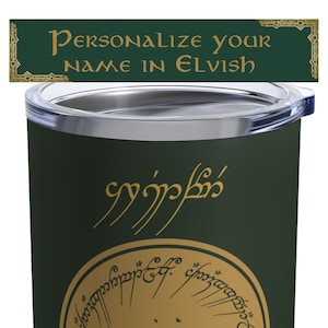 May include: A green stainless steel tumbler with a gold inscription that reads "Personalize your name in Elvish". The inscription is in a stylised font and is surrounded by a decorative border. The tumbler has a clear lid.