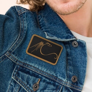May include: A person wearing a blue denim jacket with a gold and black patch featuring a dragon design.