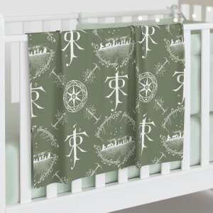 May include: A green baby blanket featuring a white pattern of the One Ring, the Elvish inscription "Ash Nazg Durbatulûk, ash nazg gimbatul, ash nazg thrakatulûk, agh burzum-ishi krimpatul", and the symbol of the White Council.