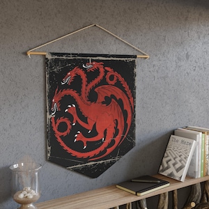 Puede incluir: Un tapiz negro y rojo con un diseño de dragón de tres cabezas. El dragón es rojo con contornos negros y está rodeado por un círculo negro. El tapiz está colgado en una pared con una barra de madera.