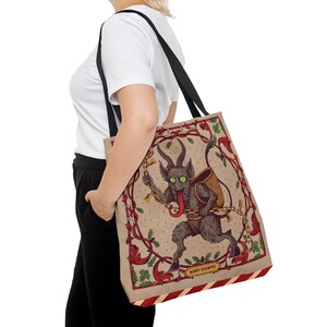 May include: A beige tote bag with a black strap features a vintage illustration of a green-eyed, red-tongued, horned creature with a sack on its back. The creature is surrounded by red and green floral designs and the text "Merry Krampus".