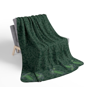 May include: A dark green throw blanket draped over a gray chair. The blanket features a repeating pattern of leaves and vines in a lighter green color. The blanket's border has a stylized leaf design.