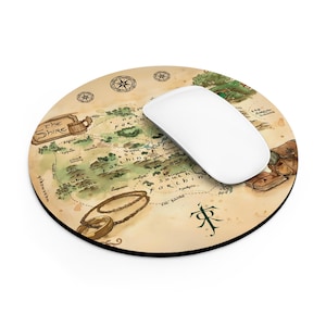May include: Round mousepad featuring a map design with a white mouse on top. The map is in shades of green, brown, and beige, with text and illustrations. The mousepad has a black border.