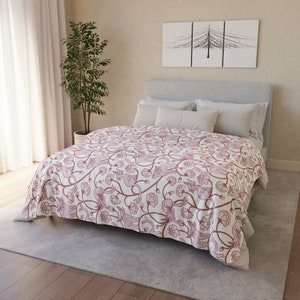 May include: A white bed with a pink floral patterned duvet cover. The bed has a white headboard and is made up with white pillows. The bed is in a bedroom with a plant in a pot and a picture on the wall.