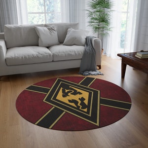 May include: A round red, black and gold rug with a diamond-shaped design featuring a stylised black bird. The rug has a distressed, vintage look.