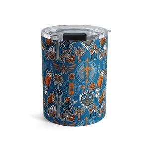 May include: A cylindrical travel mug with a clear lid and a black slider. The mug is covered in a repeating pattern of orange and white illustrations on a dark blue background. The illustrations include swords, shields, and characters.