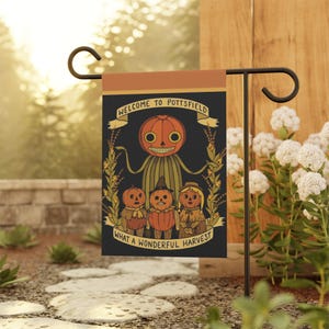 May include: A black garden flag featuring a whimsical illustration with the text "WELCOME TO POTTSFIELD" and "WHAT A WONDERFUL HARVEST". The design includes a pumpkin-headed figure and three smaller pumpkin-headed characters, surrounded by floral elements.
