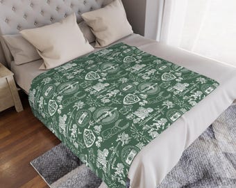 May include: A green blanket with a white pattern of shields, swords, and other heraldic symbols. The blanket is folded over a bed with white pillows and a tufted headboard. The blanket measures approximately 60 inches by 80 inches.