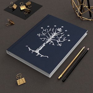 May include: A dark blue notebook with a white tree design and white stars. The notebook is closed and lying on a gray surface.