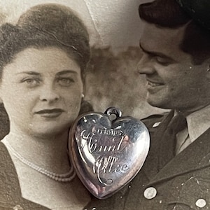 May include: A silver heart-shaped locket with the inscription "To my Aunt Ollie". The locket is in focus, while a black and white photo of a couple is blurred in the background.