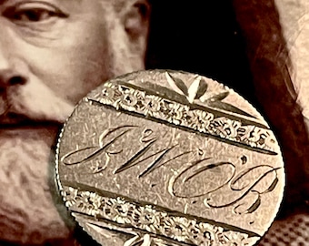 May include: A silver-toned token with the word "Mom" engraved in a cursive script. The token is surrounded by a decorative border of small flowers and leaves.