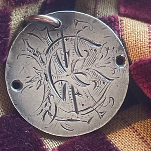 May include: A silver charm with a decorative letter C engraved on it. The charm has a loop at the top for attaching to a necklace or bracelet.