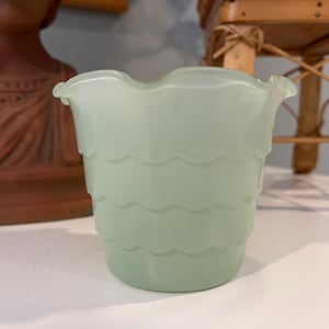 May include: A light green glass vase with a scalloped design. The vase is made of frosted glass and has a rounded shape.