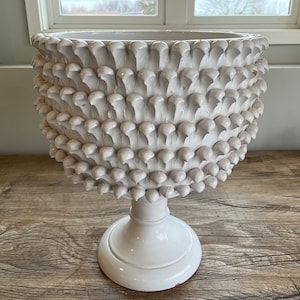 May include: White ceramic planter with a textured, spiky design resembling a pinecone. The planter has a round base and a wide, open top.