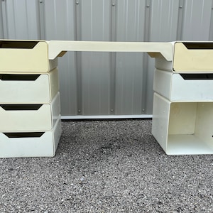 May include: A white modular desk with a white top and multiple drawers. The desk is made of plastic and has a modern design.
