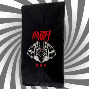 May include: Black kitchen towel with a white embroidered moth with red eyes and the text "MOTH MAN" in red.