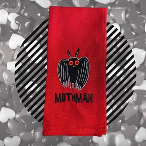 May include: Red kitchen towel with a black embroidered mothman design and the text "MOTHMAN".