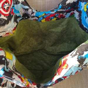 May include: A large green fabric tote bag with a superhero comic book print. The bag is open and the inside is lined with a dark green fabric.