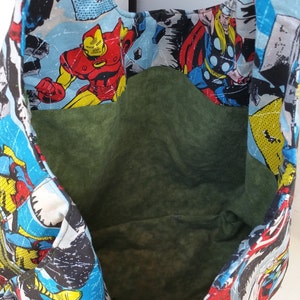 May include: A reusable tote bag made of fabric with a superhero theme. The bag features a colorful print of various superheroes, including Iron Man, Thor, and Captain America. The bag has a green lining and is perfect for carrying groceries or other items.