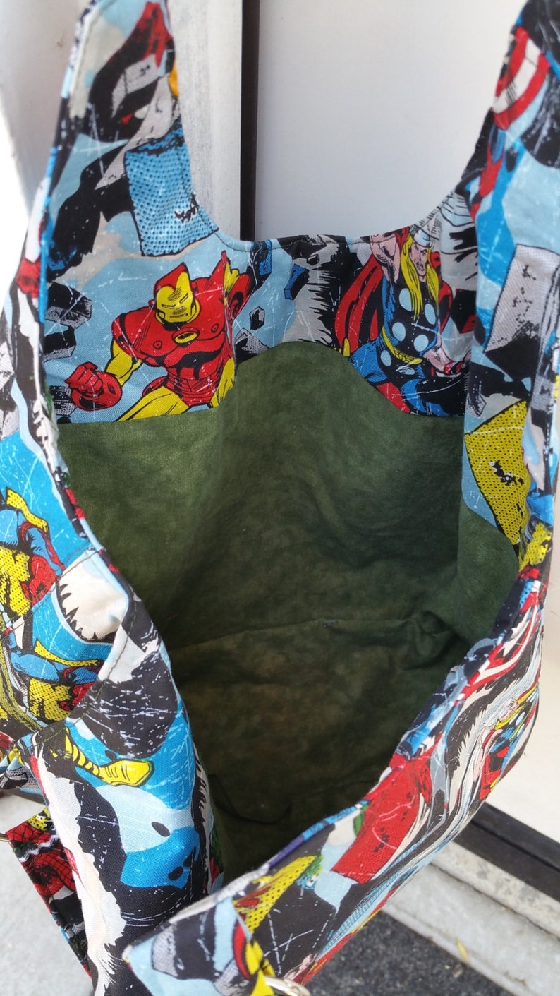 May include: A reusable tote bag made of fabric with a superhero theme. The bag features a colorful print of various superheroes, including Iron Man, Thor, and Captain America. The bag has a green lining and is perfect for carrying groceries or other items.