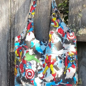 May include: A black tote bag with a colorful comic book print featuring superheroes like Iron Man, Captain America, and Thor. The bag has two long straps.