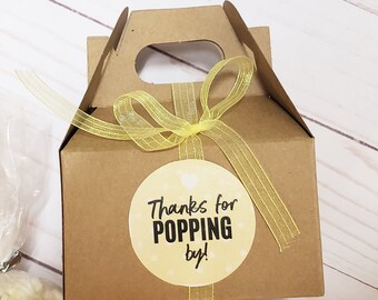 May include: A brown cardboard box with a yellow ribbon and a round sticker that says "Thanks for POPPING by!" The box is filled with popcorn.