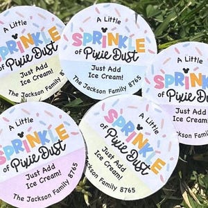 May include: Five circular stickers with the text "A Little Sprinkle of Pixie Dust" in colourful letters. The stickers also say "Just Add Ice Cream!" and "The Jackson Family 8765". The background is green grass.
