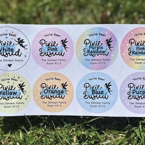 May include: Sheet of eight circular stickers with pastel backgrounds and the words "You've Been Pixie Dusted." Each sticker has a different color and the text "The Johnson Family Room 6713."