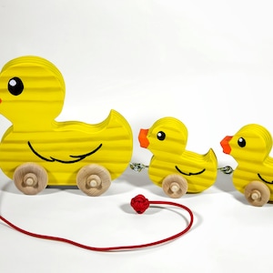 May include: A set of three yellow wooden toy ducks on wheels. The largest duck is connected to a red string, and the ducks are all facing the same direction.