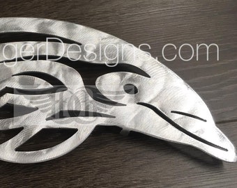 May include: A silver metal dolphin sculpture with a tribal design. The sculpture is made of metal and has a brushed finish. The dolphin is facing to the right and has a stylized tail.