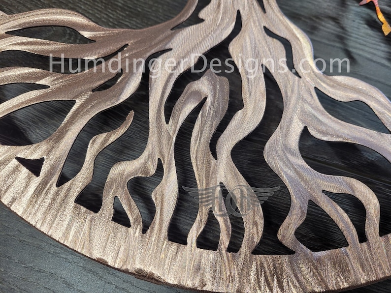 K&ouml;nnte beinhalten: Ein Wandkunstwerk aus Metall in Form eines Baumes mit einer braunen, metallischen Oberfl&auml;che. Der Baum hat ein gro&szlig;es, kompliziertes Wurzelsystem mit einem Ausschnittmuster. Der Hintergrund ist eine dunkle Holzoberfl&auml;che. Der Text "HumdingerDesigns.com" ist im Bild sichtbar.