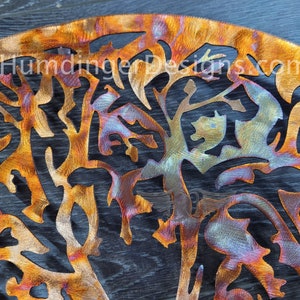 K&ouml;nnte beinhalten: Ein Wandkunstwerk aus Metall, das einen Baum mit filigranen &Auml;sten und Bl&auml;ttern darstellt. Das Metall wurde behandelt, um eine farbenfrohe, irisierende Oberfl&auml;che mit Orange-, Blau- und Violettt&ouml;nen zu erzeugen.