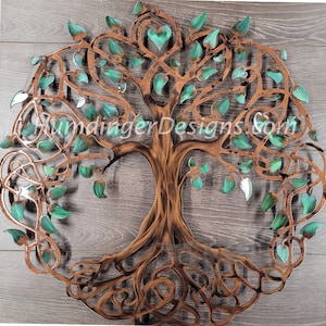 May include: A metal tree of life wall art with a brown and copper finish. The tree has a large trunk and intricate branches with green leaves. The roots are also intricately designed.