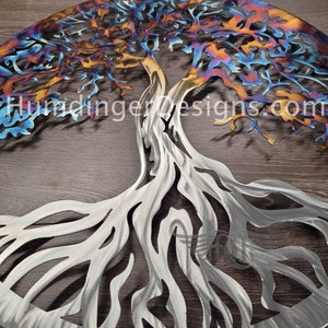 May include: A metal wall art sculpture of a tree with intricate branches and roots. The tree is made of steel and has a rainbow-like finish. The sculpture is circular and has a diameter of approximately 24 inches.