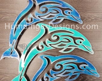 May include: Three metal dolphin sculptures with a tribal design. The dolphins are layered on top of each other and are painted in shades of blue and green.